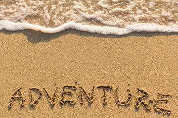 Adventure - inscription on sand beach with the soft wave.