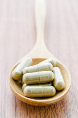 Herb capsule in wooden spoon.