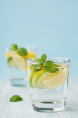 Mineral infused water with limes, lemons, ice and mint leaves on blue background, homemade detox soda water recipe