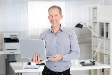 Obraz premium Confident Businessman Holding Laptop In Office