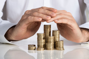 Businessman Protecting Stacked Coins At Desk