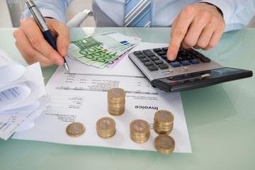 Businessman Calculating Invoice With Money At Desk