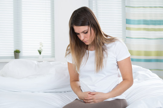 Woman With Stomach Ache Sitting On Bed