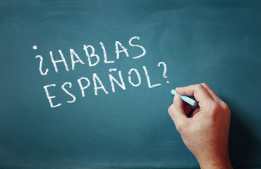 the question do you speak espanol written on chalkboard and male hand
