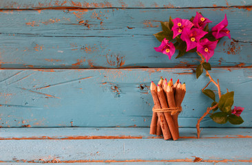 stack of wooden colorful pencils on wooden texture table next to purple bougainvillea flower
