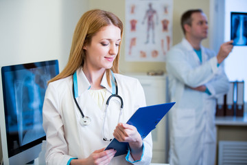 Portrait of friendly confident doctors in hospital. Enthusiastic medical staff at work. Female doctor with stethoscope writing on the tablet. 