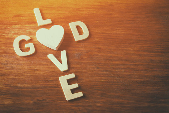 selective focus photo of The words love is god made with block wooden letters on wooden background. religion concept. vintage filtered and toned
