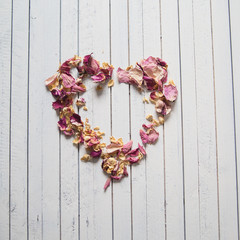 Vintage heart made of dried petals on wooden white background