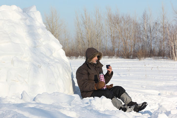 The man sitting near an igloo and drinking tea from thermos  in the winter
