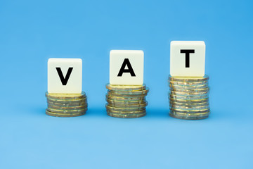 VAT (Value Added Tax) on stacks of gold coins over blue background