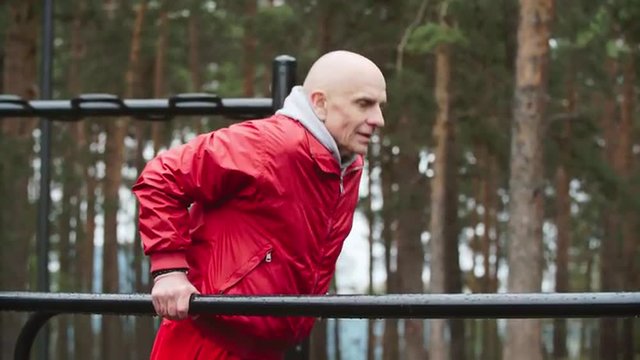 Senior man doing dips on parallel bars in the park