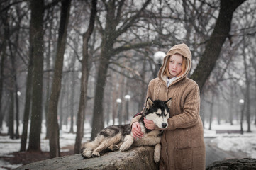 Naklejka na ściany i meble A teen girl stand with husky dog near a big stone in winter