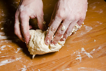 Men's hands knead the dough on the wooden table. The chef prepares the dough for Italian cuisine.