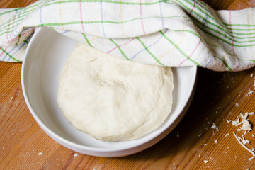 The dough in the bowl under a towel. Preparations for baking the dough in a rustic style.