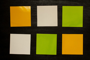 Yellow, white and green square stickers for notes on a black background