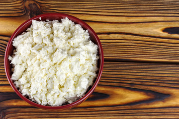 Fresh cottage cheese in ceramic bowl on wooden table, top view