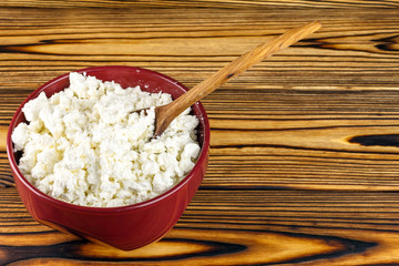 Fresh cottage cheese in ceramic bowl and spoon on wooden table, with space for text