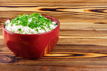 Fresh cottage cheese with sour cream, dill, parsley, onion in ceramic bowl on wooden table, space for text