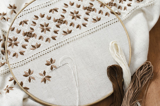 The wooden hoop with the embroidery pattern of brown and beige color on canvas, on wooden table.Rustic style. Selective focus.