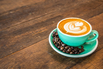 Latte hot coffee in green cup with latte art and roasted coffee beans. Wooden table background. In coffee shop.