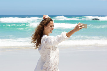 Fototapeta na wymiar Smiling young woman taking selfie at the beach