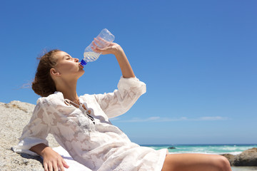 Young woman drinking water from bottle at the beach
