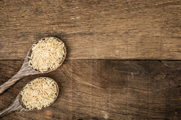 Brown rice on wooden spoon. Wooden background. Top view.
