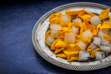 Rose petals with ice cubes in the metal plate on the blue stone table