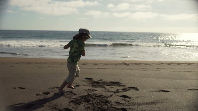 Young boy dancing on the sandy beach and having fun, steadycam shot

