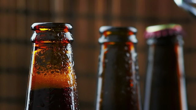 man uncap three bottles of fresh beer with foam and drops on dark background pub dolly camera movement