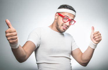Fototapeta premium Funny nerd doing aerobics and showing thumbs up. Isolated on gray background, studio shot.