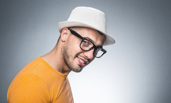Portrait of trendy young man, isolated on gray. Close up gorgeous guy with hat and eyeglasses