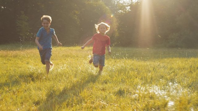 Two happy kids running competition over field in sunshine
