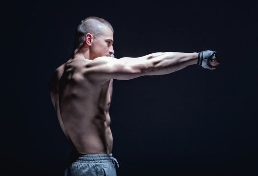 side view of male fighter makes punch on black background