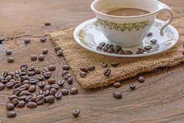 Classic Coffee cup with saucer and wooden spoon and pile of coffee beans on a wooden table
