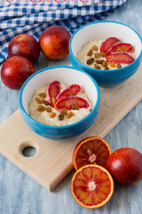 Tasty oatmeal with sicilian orange slices and raisins on blue bowls on wooden background