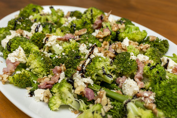 Close up of fresh broccoli salad with bacon, feta cheese and walnuts drizzled with olive oil and...