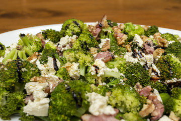 Close up of fresh broccoli salad with bacon, feta cheese and walnuts drizzled with olive oil and good quality balsamic vinegar.
