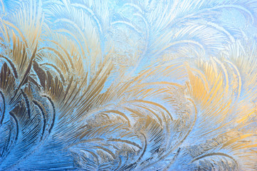 Window glass covered with ice pattern against sunset