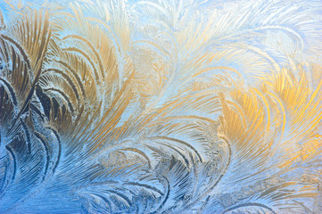 Window glass covered with ice pattern against sunset