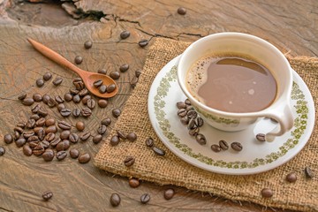 Coffee cup with saucer and wooden spoon and pile of coffee beans on a wooden table
