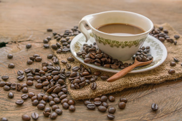 Coffee cup with saucer and wooden spoon and pile of coffee beans on a wooden table
