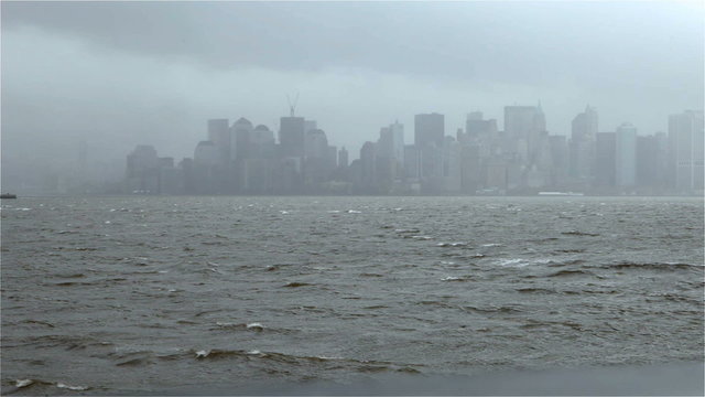 Video footage on a cold and windy winters day looking over the choppy waters towards the NYC skyline shrouded in a misty blanket in the distance. Strong winds and raining weather conditions.