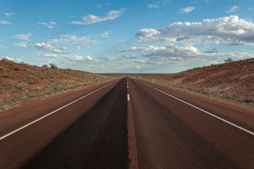 A road with goes straight until the horizon. Converging lines, blue sky and clouds making it a strong road trip image.