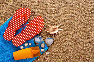 Flip-flops, sunscreen spray and towel on the beach.