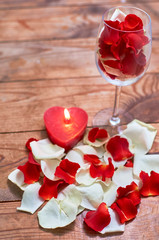 Fototapeta na wymiar red candle with red rose petals in glass on wooden background