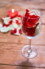 red candle with red rose petals in glass on wooden background