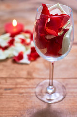 red candle with red rose petals in glass on wooden background