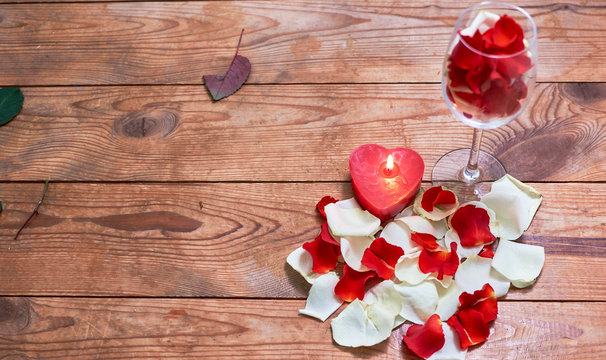 red candle with red rose petals in glass on wooden background