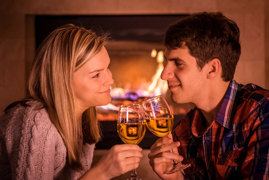 Happy young couple sitting near fireplace and drinking wine